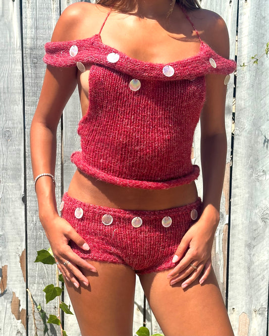 Model wearing Bailey Prado handmade red knit two-piece seashell set with shell embellishments in golden hour light.