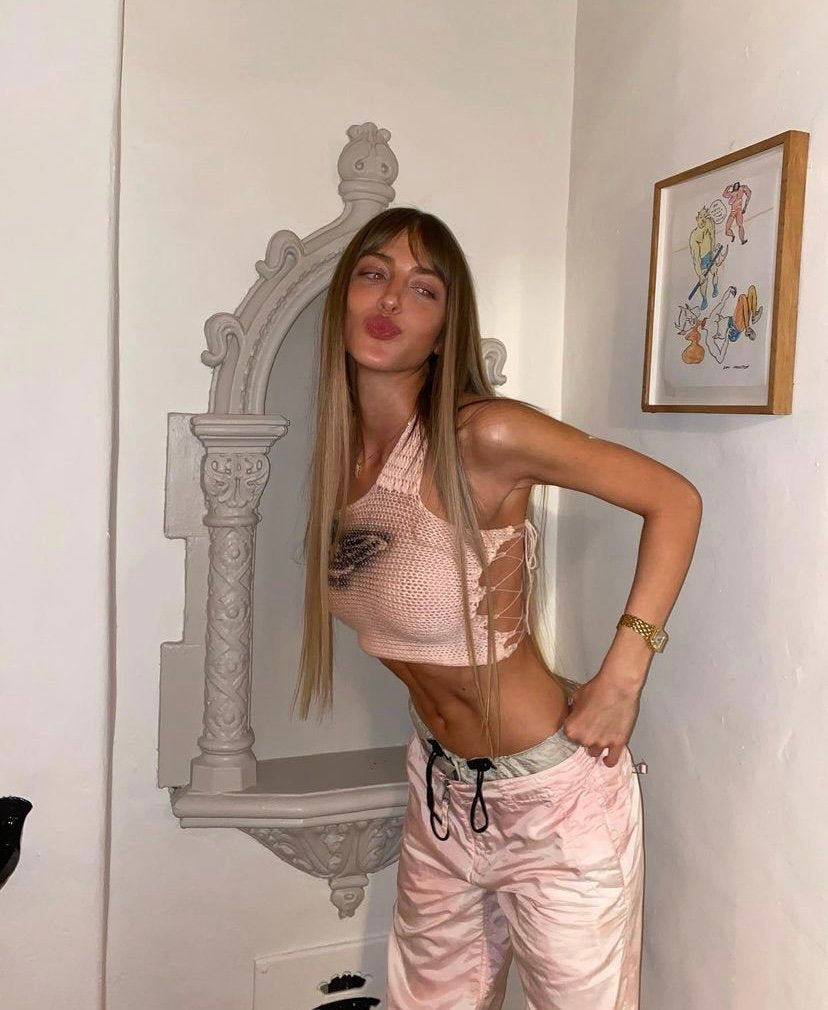Model wearing the Bailey Prado Butterfly Tank, a one-shoulder crochet crop top with a hand spray-painted butterfly motif and side lace-up closure.