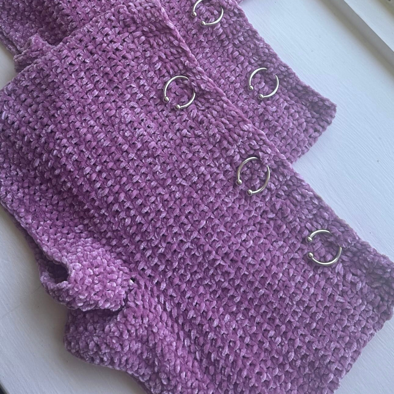 Close-up of the hand-crocheted texture, silver horseshoe barbell hardware, and adjustable button closure on the Bailey Prado Lilac Horseshoe Shorts.