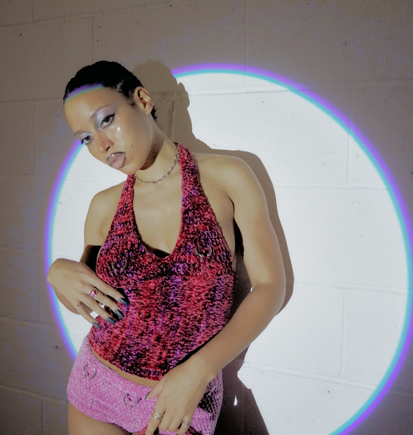 Model wearing the Bailey Prado Piercing Tank, a burgundy crochet halter top with silver piercing-inspired hardware and an adjustable lace-up back.