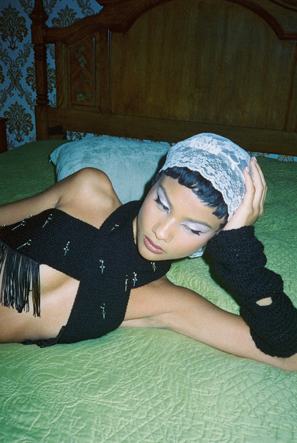 Model wearing the Bailey Prado Tassel Charm Top, a black wrap halter top with silver star charms and dramatic tassel trim.