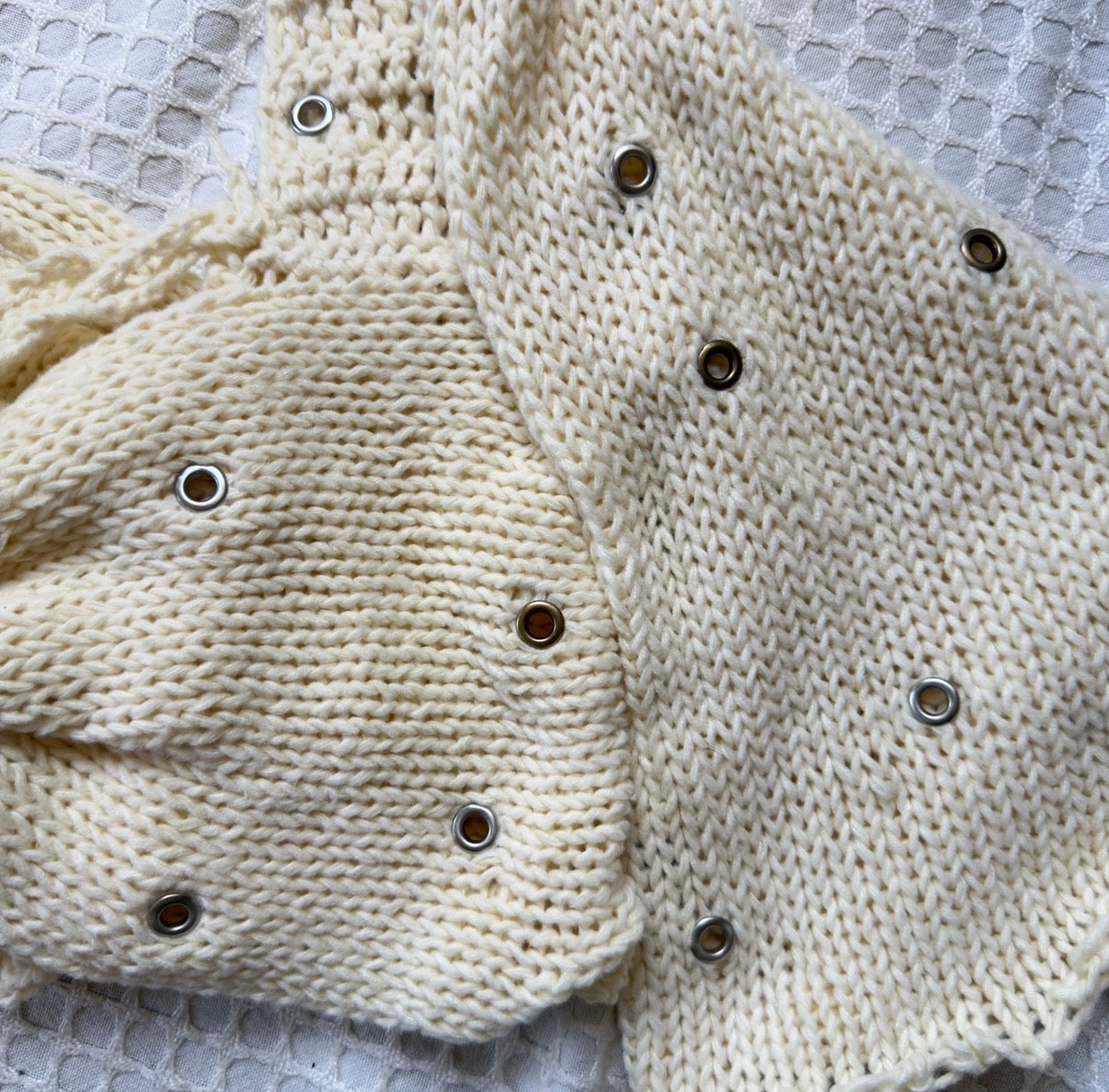 Handmade cream knit bow top with eyelet embellishments by Bailey Prado, photographed on a white background.